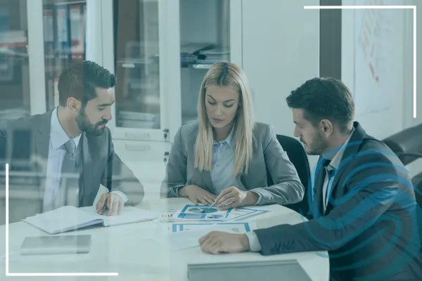 This is an image of 3 professional people, 2 men and 1 woman, sitting around a table reviewing details on a document.  They are engaged in their conversation.  There is also a Specialized Recruiting Group logo on the image.